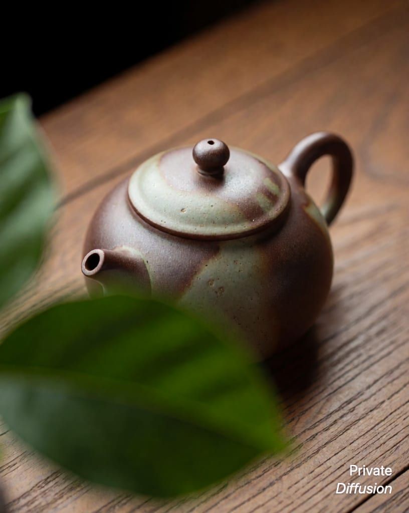 a ceramic teapot on a wooden table, with partly hidden added