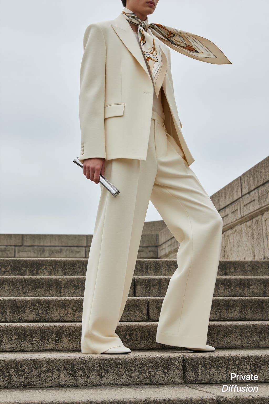 An adult model poses in an ivory suit on concrete steps.